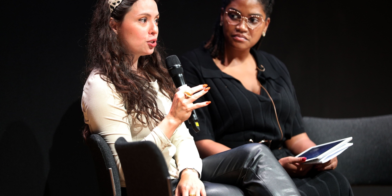 Sophie Smith Gellar sat on stage holding a microphone. To her right is Whitney Simon